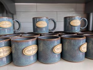 Stacked Chef's Corner mugs. blue ceramic with tan logo.