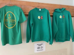 Three green Chef's Corner Logo shirts hanging on a wall